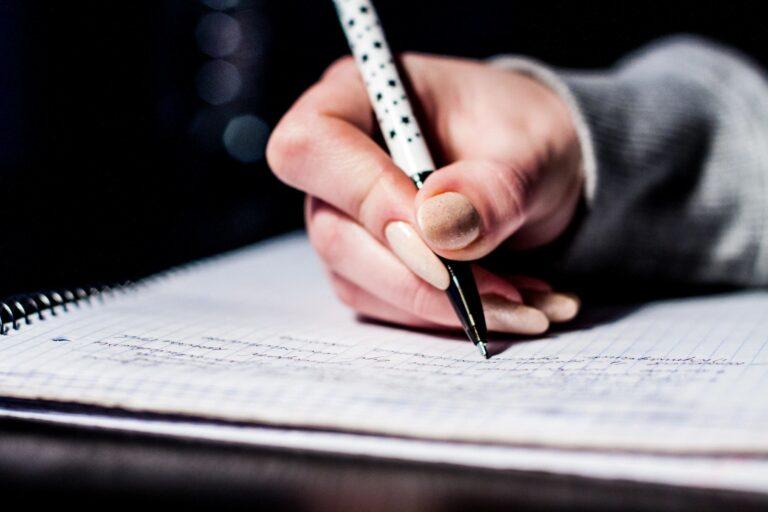 a white hand writing on a piece of paper.